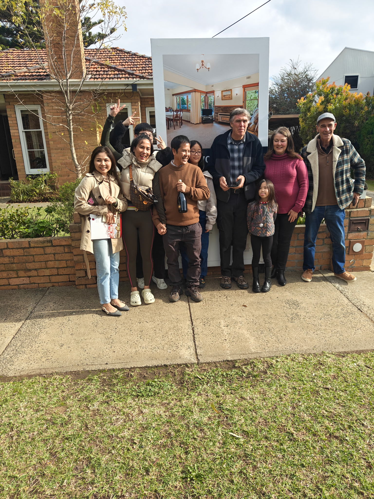 A group of Melbourne property clients celebrating beside a sold property board